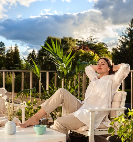 Beautiful young girl relaxing and enjoying sun while having tea, sitting at balcony at sunlight at summer. Slow living, tranquil moment, mental health. Backyard terrace vacation.
