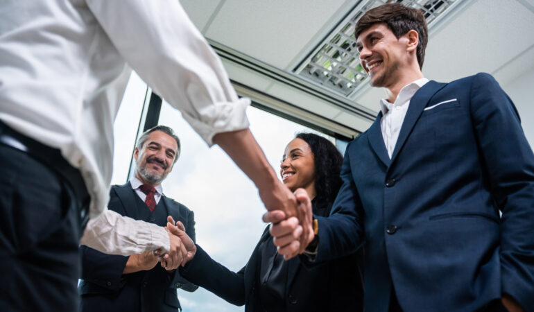 Caucasian businessman making a handshake together while stand in office. Attractive team of employee worker enjoy partnership agreement after negotiations for business deal during working in corporate