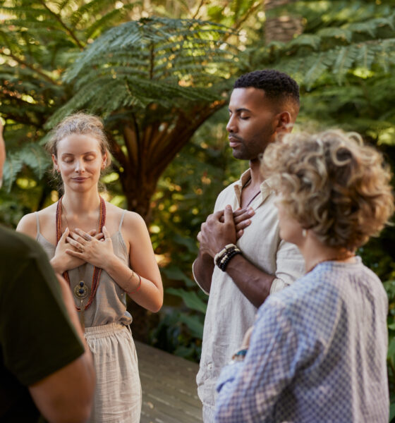 Group of multiethnic adults standing peacefully in circle with hands on their hearts during a wellness retreat in nature. Diverse people practice mindfulness and gratitude together in a forest. Mixed race group sharing a meditation on fourth chakra, heart chakra, outdoor with copy space.