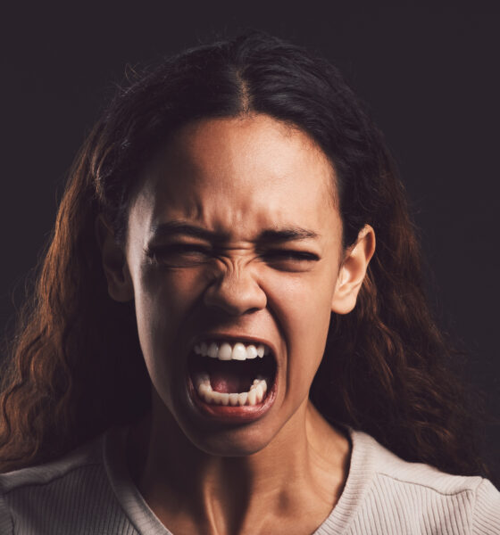 Shot of a young woman experiencing mental anguish and screaming against a black background.