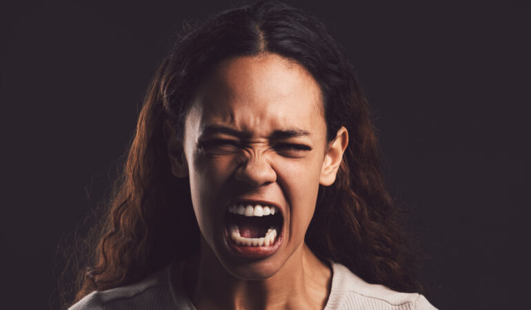 Shot of a young woman experiencing mental anguish and screaming against a black background.