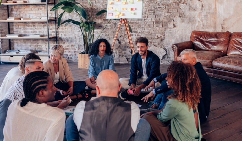 Coworkers discussing new ideas sitting on the floor in a circle during a brainstorming meeting